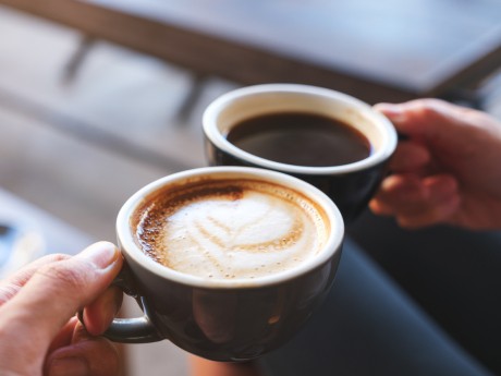 Closeup image of a man and a woman clinking white coffee mugs in cafe