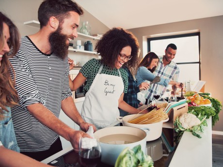 Large group of six happy friends preparing food for a pasta cooking class at table at home or in a small culinary school