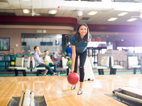 Full length of smiling teenage girl throwing ball while training for bowling in club